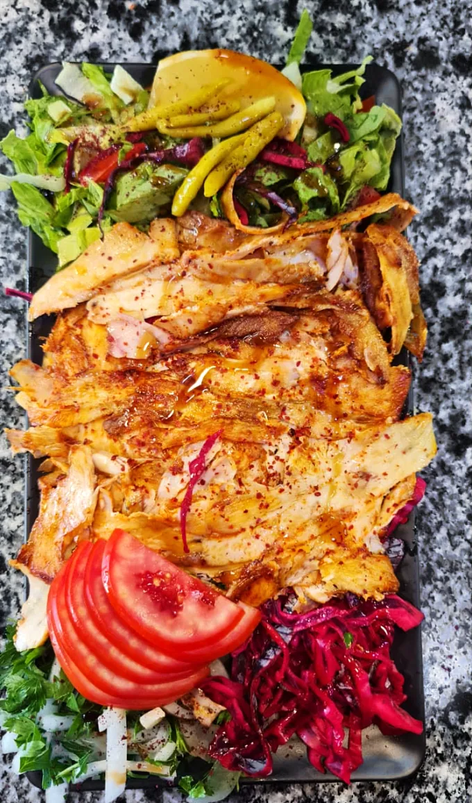 Tabakta porsiyon tavuk döner; yeşillik, domates, kırmızı lahana turşusu ve limon