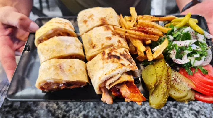 Elde tutulan tabakta dilimlenmiş lavaş döner, patates kızartması, soğan piyazı, turşu ve domates